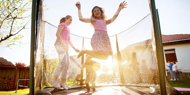 Dvoje dece sa majkom skaču i zabavljaju se na trambolini u dvorištu