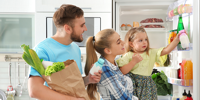 Srećna porodica sa detetom uzima namirnice sa vrata kombinovanog frižidera