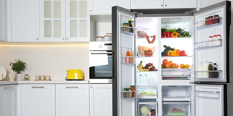 U kuhinji se nalazi otvoreni side by side frižider sive boje sa namirnicama smeštenim na policama i fiokama 