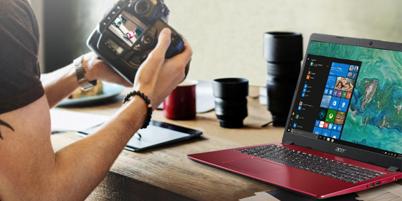 Momak drži digitalnu kameru i sedi za radnim stolom na kome se nalazi Acer laptop crvene boje