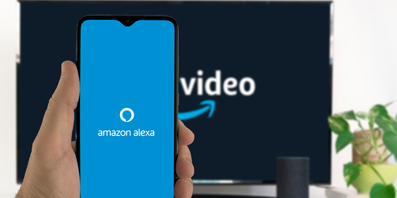 Muškarac drži u ruci mobilni telefon i glasovnim porukama putem Amazon Alexa asistenta upravlja televizorom
