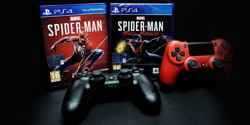 Dva džojstika crvene i crne boje naslonjeni su na dve Spider-Man PS4 igrice