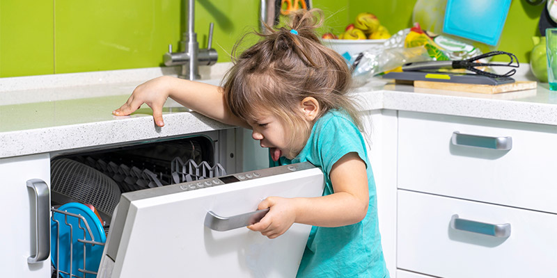 Devojčica u plavom kompletiću otvara mašinu za sudove iz koje se oseća loš miris