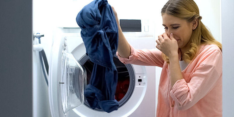 Žena izvlači veš iz mašine za pranje veša i zapušila je nos zbog neprijatnog mirisa