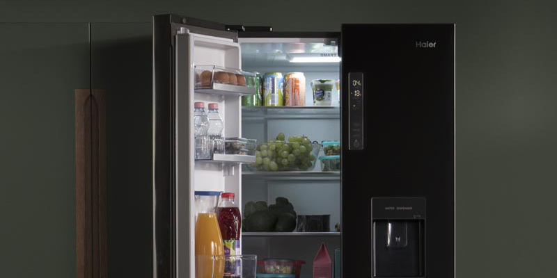 Na Haier Side by side frižideru sive boje sa digitalnim displejom otvorena su jedna vrata iz kojih se krije mnoštvo svežih namirnica – grožđe, jaja, mleko, sokovi u flasama i limenkama