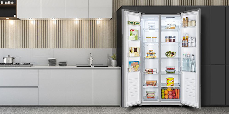 U savremenoj kuhinji nalazi se Hisense Side by side frižider RS560N4AD1 čija su vrata širom otvorena. Njegove mnogobrojne police i fioke ispunjene su raznim namirnicama