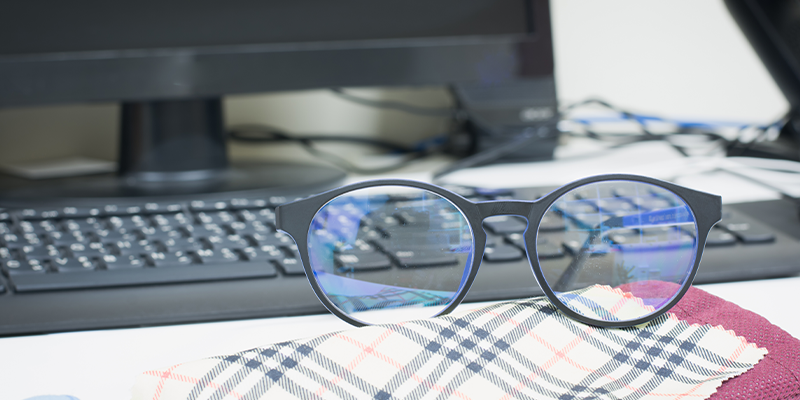 Zaštitne naočare za kompjuter sa crnim okvirom položene na sto, na staklima se vidi plavi odsjaj