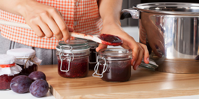 Na kuhinjskom pultu, ženske ruke sipaju džem od šljiva u teglice