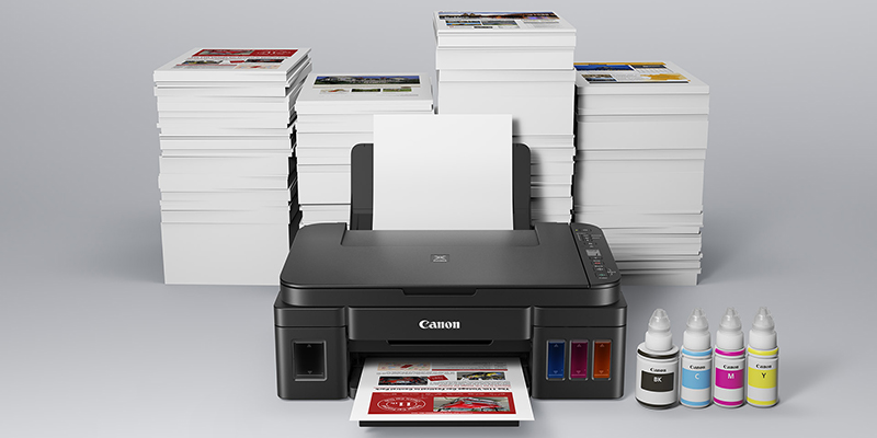 Canon Pixma štampač okružen velikom gomilom ištampanih papira i bojama u bočicama