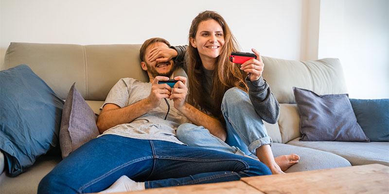 Mladi par sedi na krevetu i igra igrice koristeći Nintendo Switch konzolu