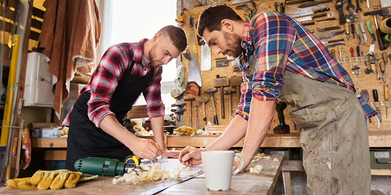 Dva muškarca u radionici savijeni nad radnim stolom nešto popravljaju