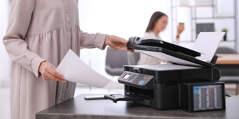 Devojka u lila haljini koristi multifunkcionalni štampač za skeniraje dokumenta na poslu