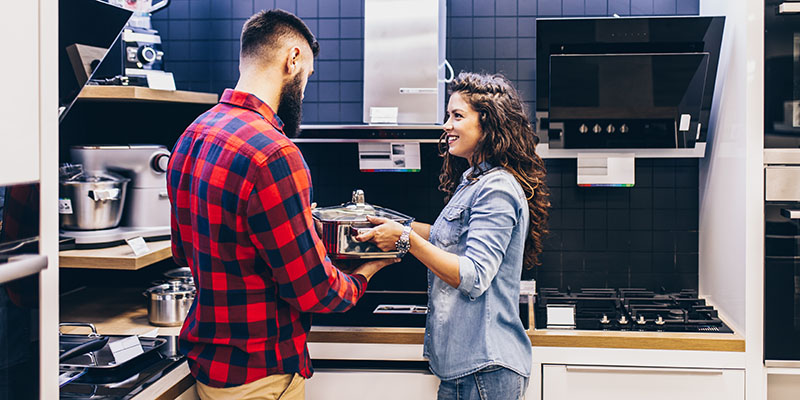 Momak i devojka pokušavaju da odaberu novo posuđe za svoju kuhinju, devojka drži jednu šerpu kao prvi izbor