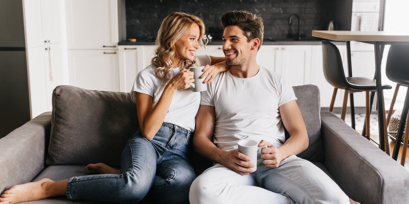 Dečko i devojka sede na kauču, nasmejani i piju kafu zajedno