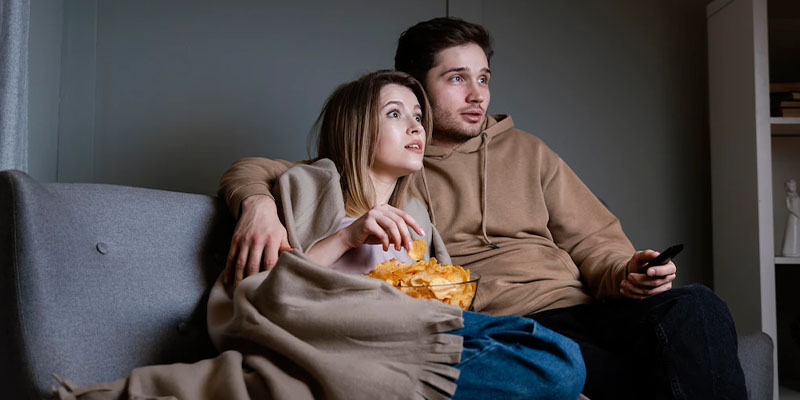 Dečko i devojka zagrljeni gledaju TV