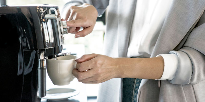 Žena u sivom sakou pravi kafu na aparatu