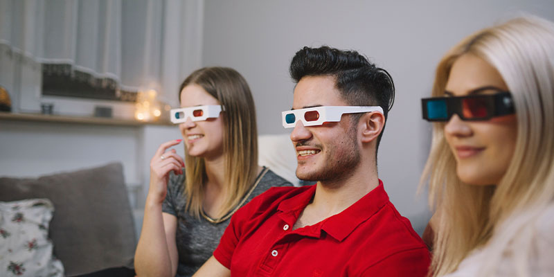 Društvo, momak i dve devojke uživaju u gledanju 3D filma koristeći projektor i 3D naočare