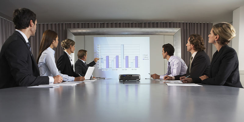Zaposleni sede u sali za sastanke i gledaju u prezentaciju prikazanu pomoću projektora na projektorskom platnu