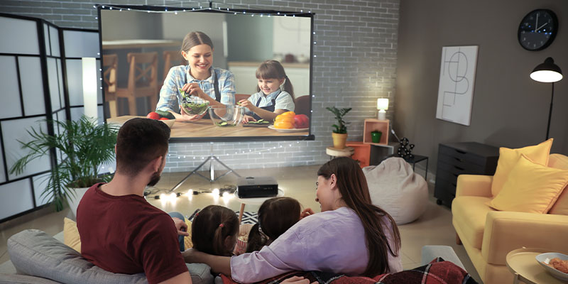 Porodica uživa gledajući film na projektorskom platnu koristeći svoj projektor za kućni bioskop
