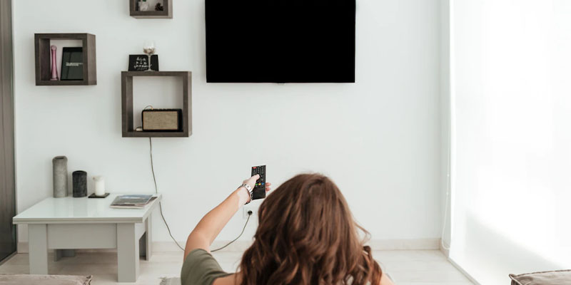 Devojka uključuje TV koji je okačen na zid u sobi