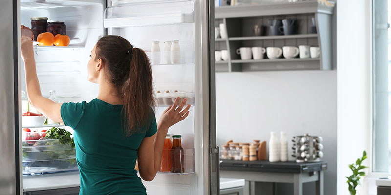 Devojka vadi namirnice iz kombinovanog frižidera sa zamrzivačem dole
