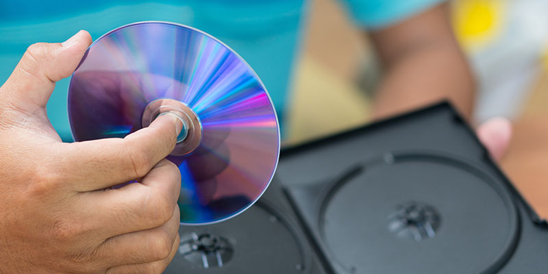 Muška ruka drži u ruci DVD disk koji je upravo izvađen iz svoje kutije