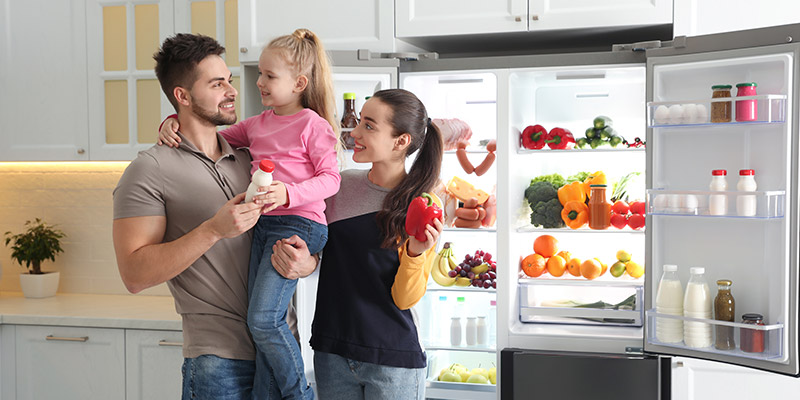 Nasmejani tata, mama i devojčica uzimaju namirnice iz side by side frižidera u sivoj boji