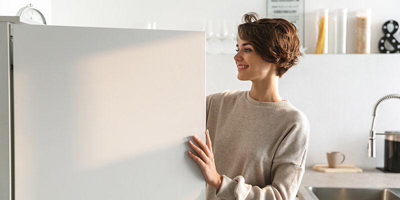 Nasmejana žena otvara vrata frižidera