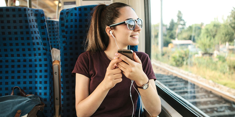 Nasmejana devojka sluša muziku putem slušalica i uživa u putovanju vozom