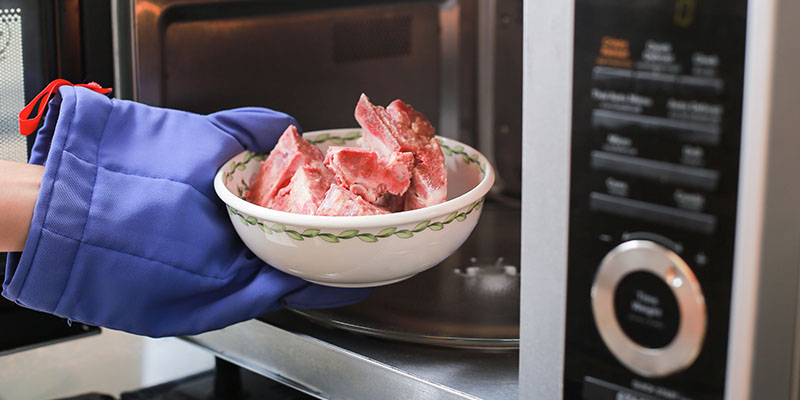Osoba stavlja činiju zamrznutog mesa u mikrotalasnu rernu