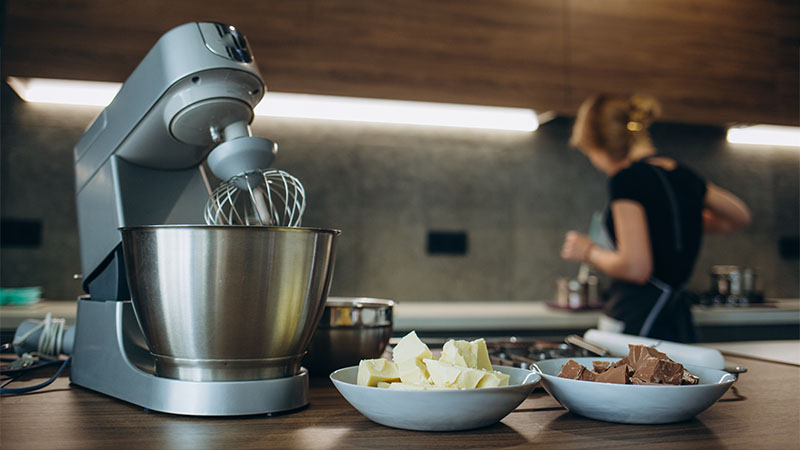 Žena priprema fil na šporetu, dok kuhinjski robot obavlja proces mućenja druge smese