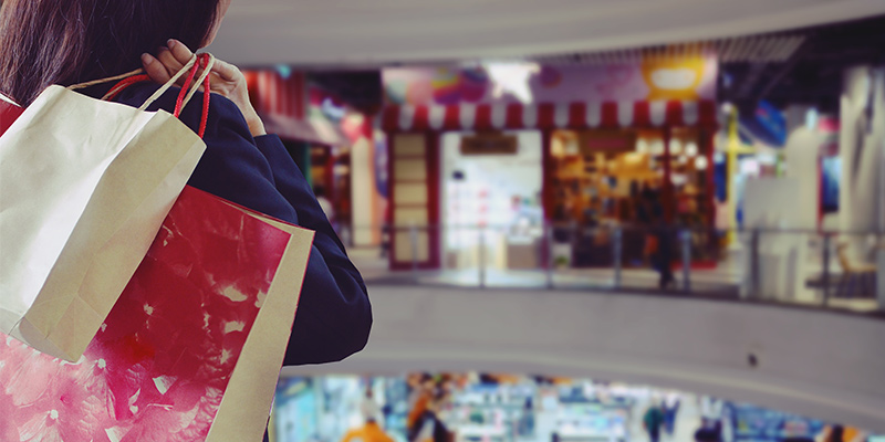 Žena u shopping centru slikana sa leđa, nosi kese iz šopinga