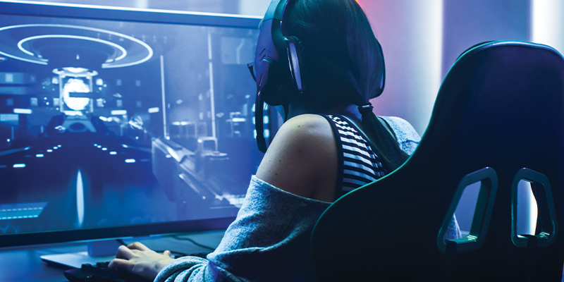Devojka gejmerka, sa slušalicama, sedi ispred monitora i igra igrice